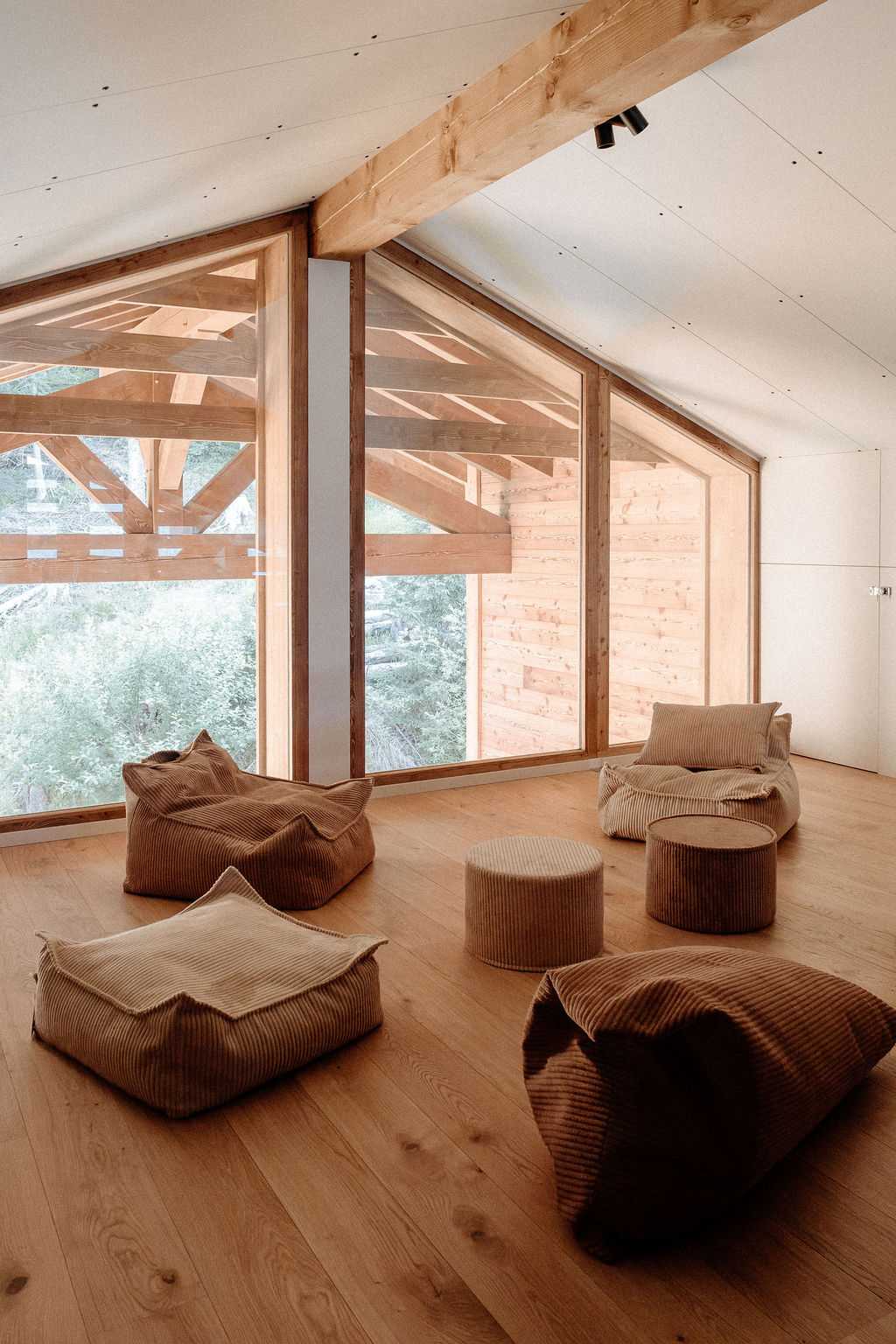 Mezzanine avec poufs face à de grandes baies vitrées triangulaires donnant sur les arbres